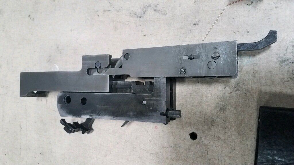 Disassembled firearm trigger mechanism, metal parts on a light surface.