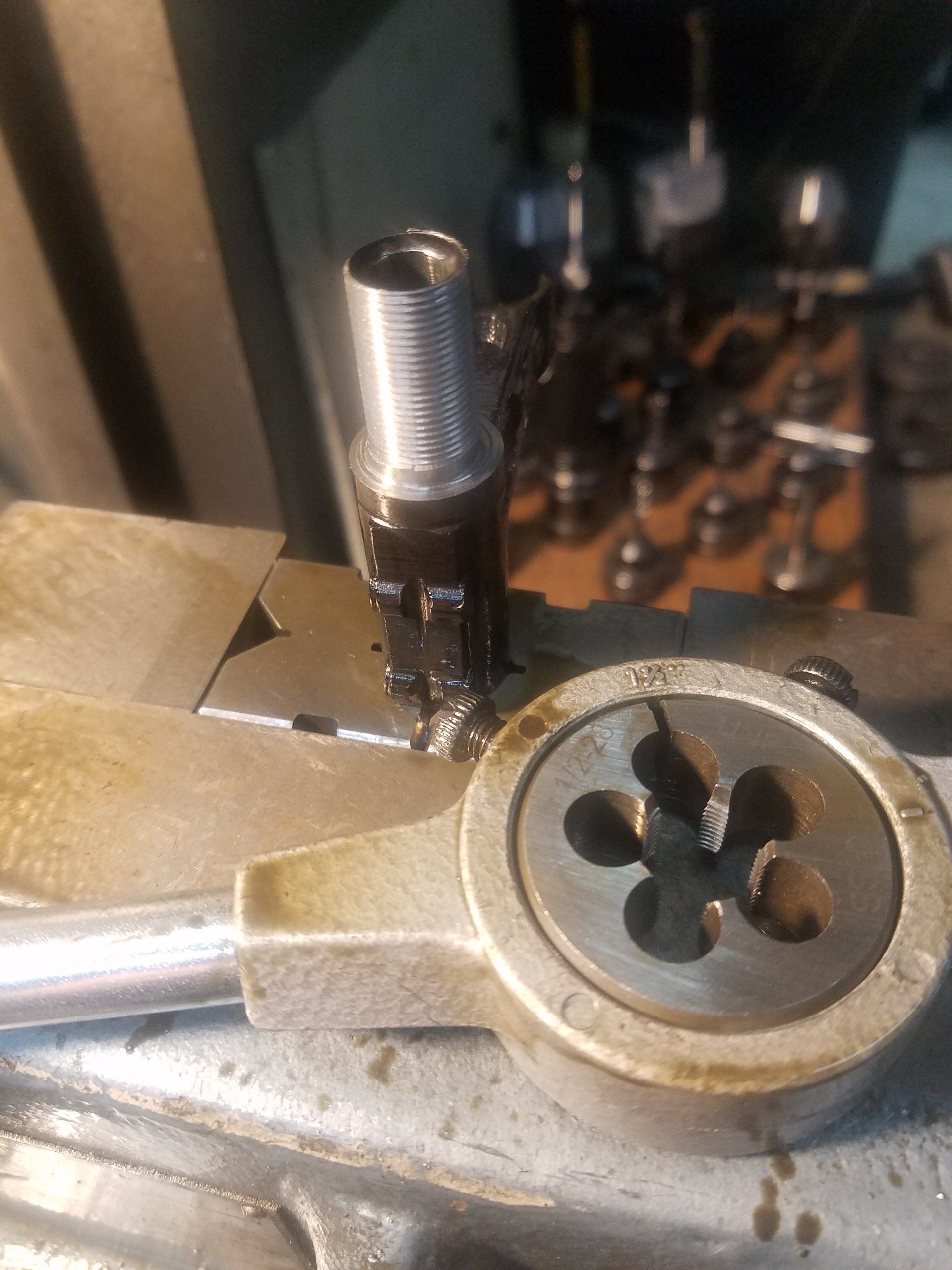 A metal screw being threaded with a die, tool in a workshop.