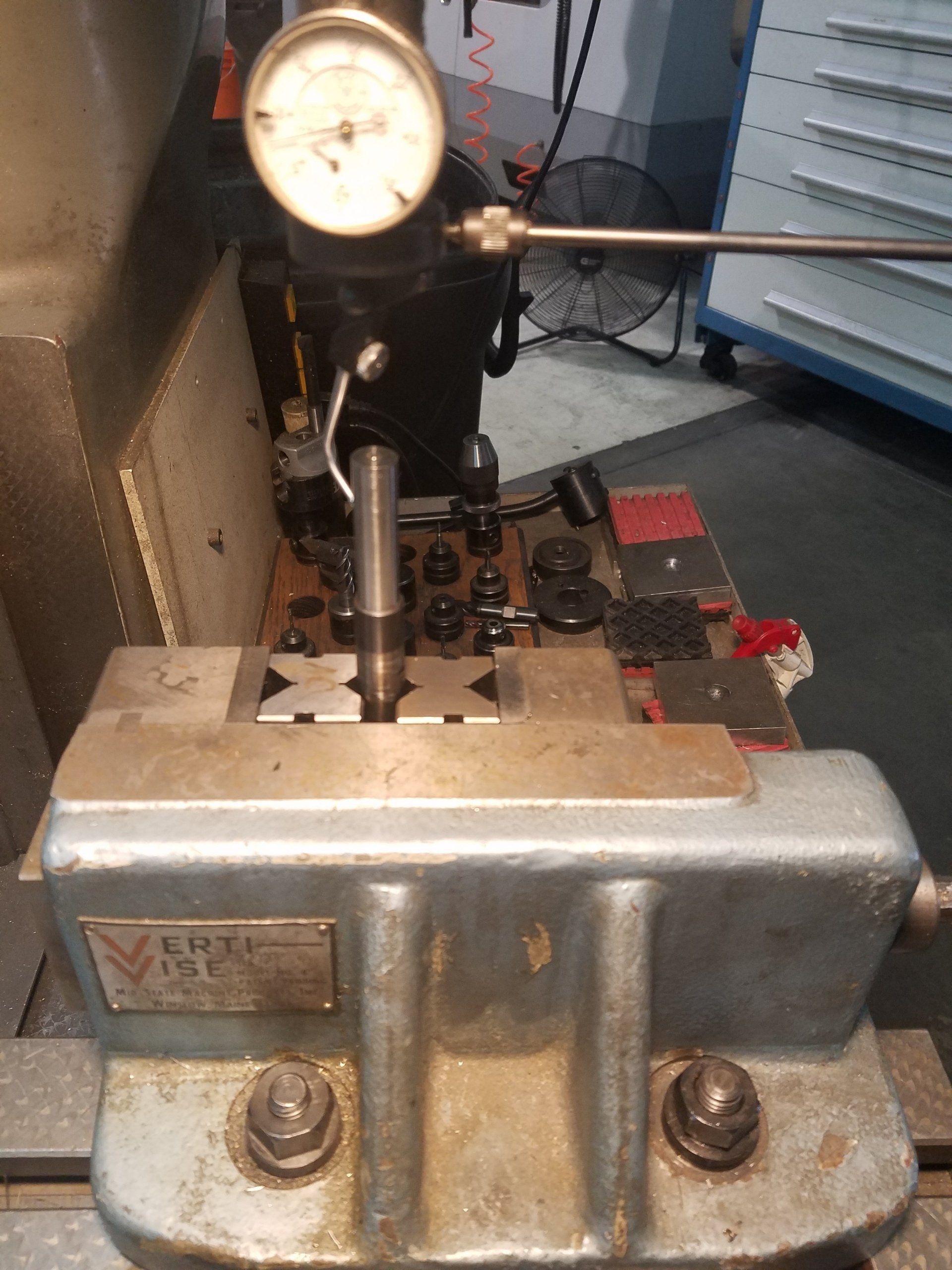 Dial indicator measuring tool set up on a vise with metal parts in a workshop.