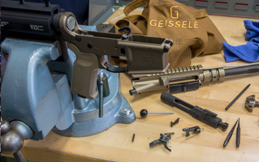 A disassembled rifle being worked on in a workshop, with various parts scattered around.