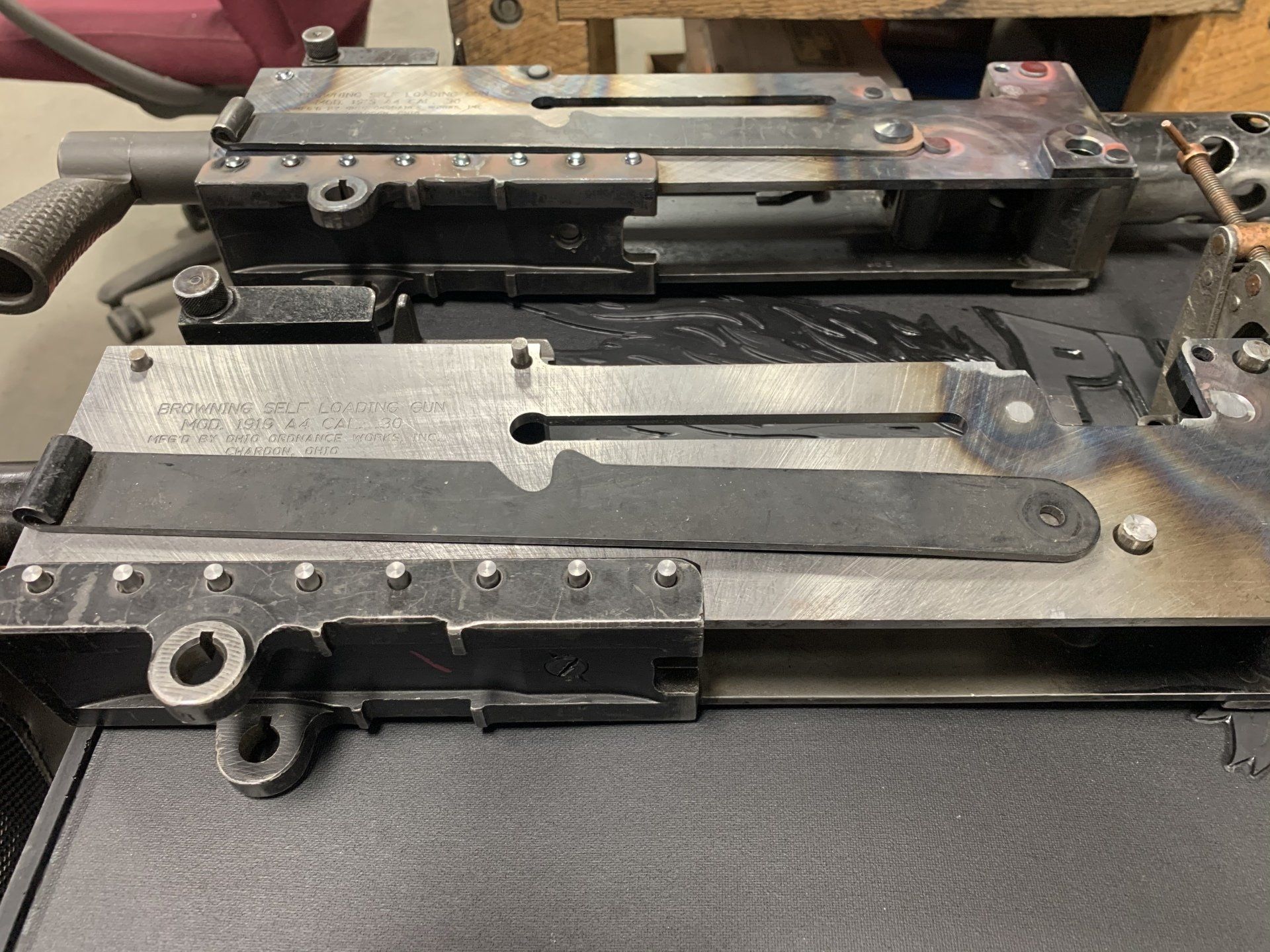 Metal components of a machine gun frame, likely in a workshop, show welds and unfinished parts.