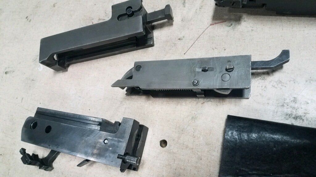Disassembled firearm parts on a surface, including receivers, trigger assembly, and other components.