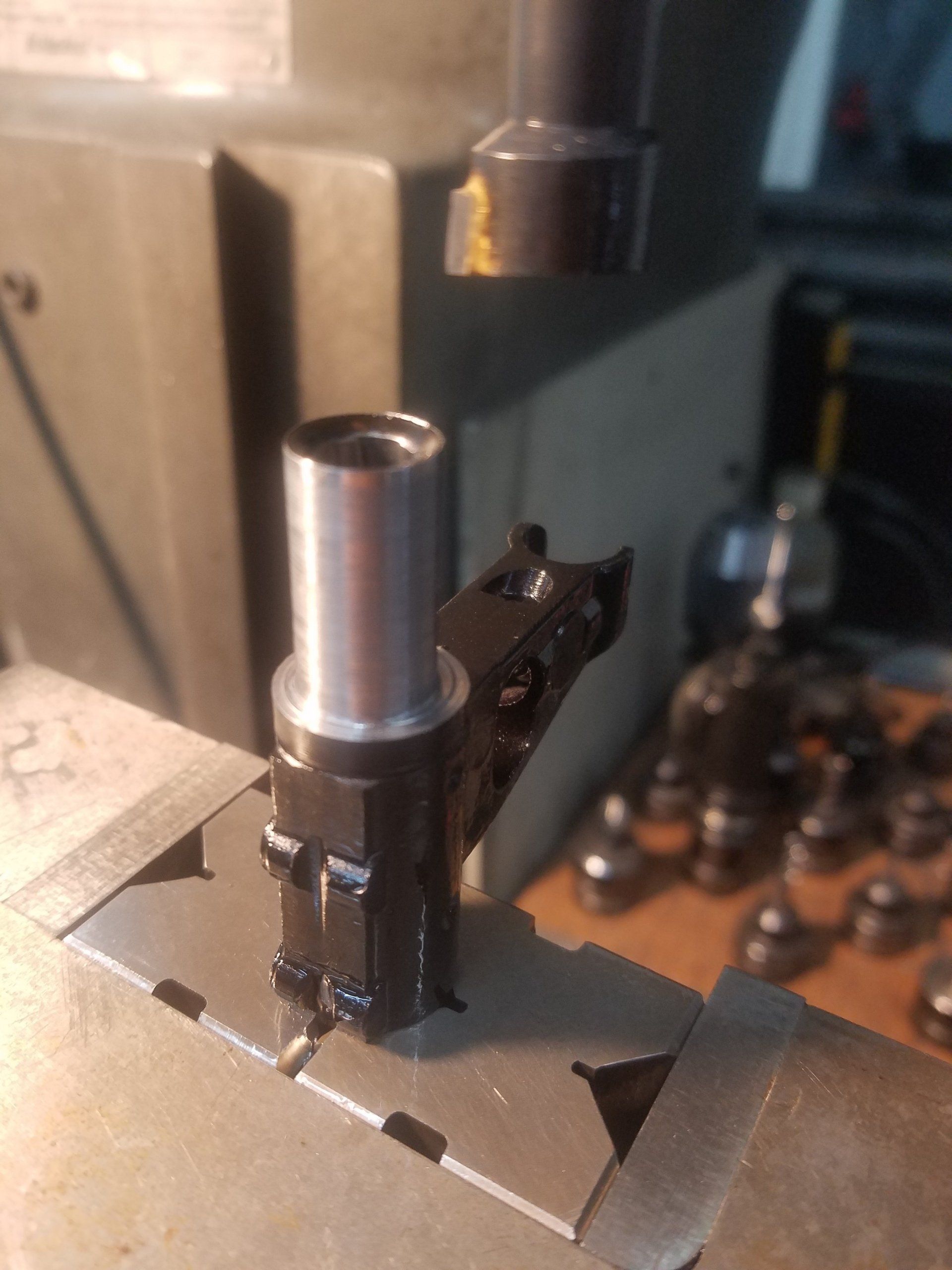 Black metal part with silver cylinder held in a vise, next to milling machine.