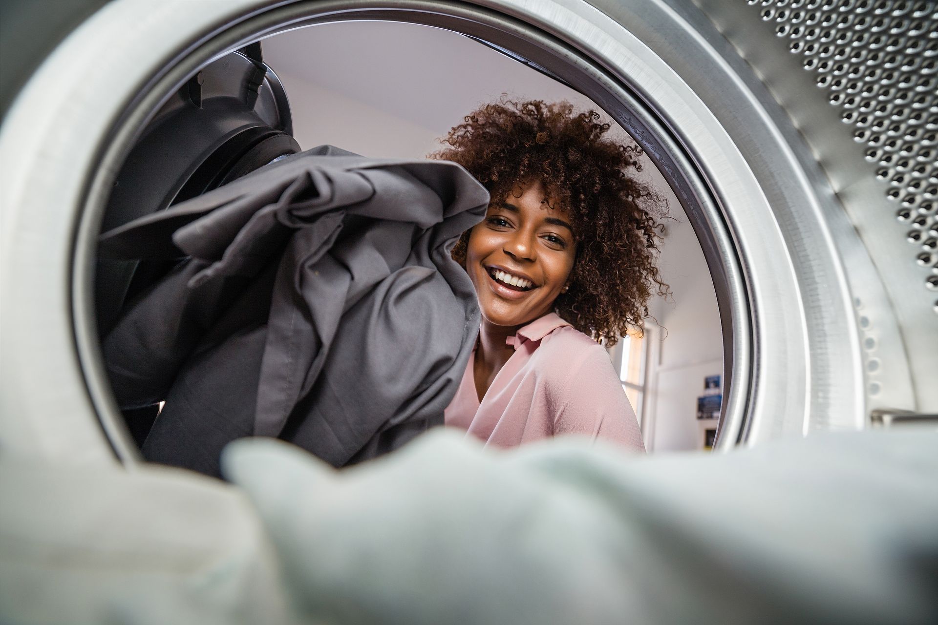 Woman with curly hair smiles while putting clothes in a washing machine