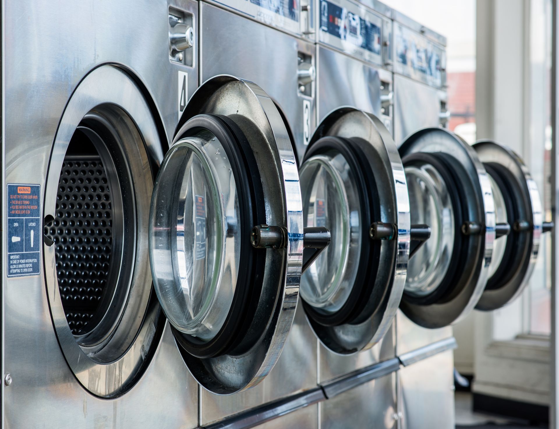 Row of commercial washing machines with open doors in a laundromat