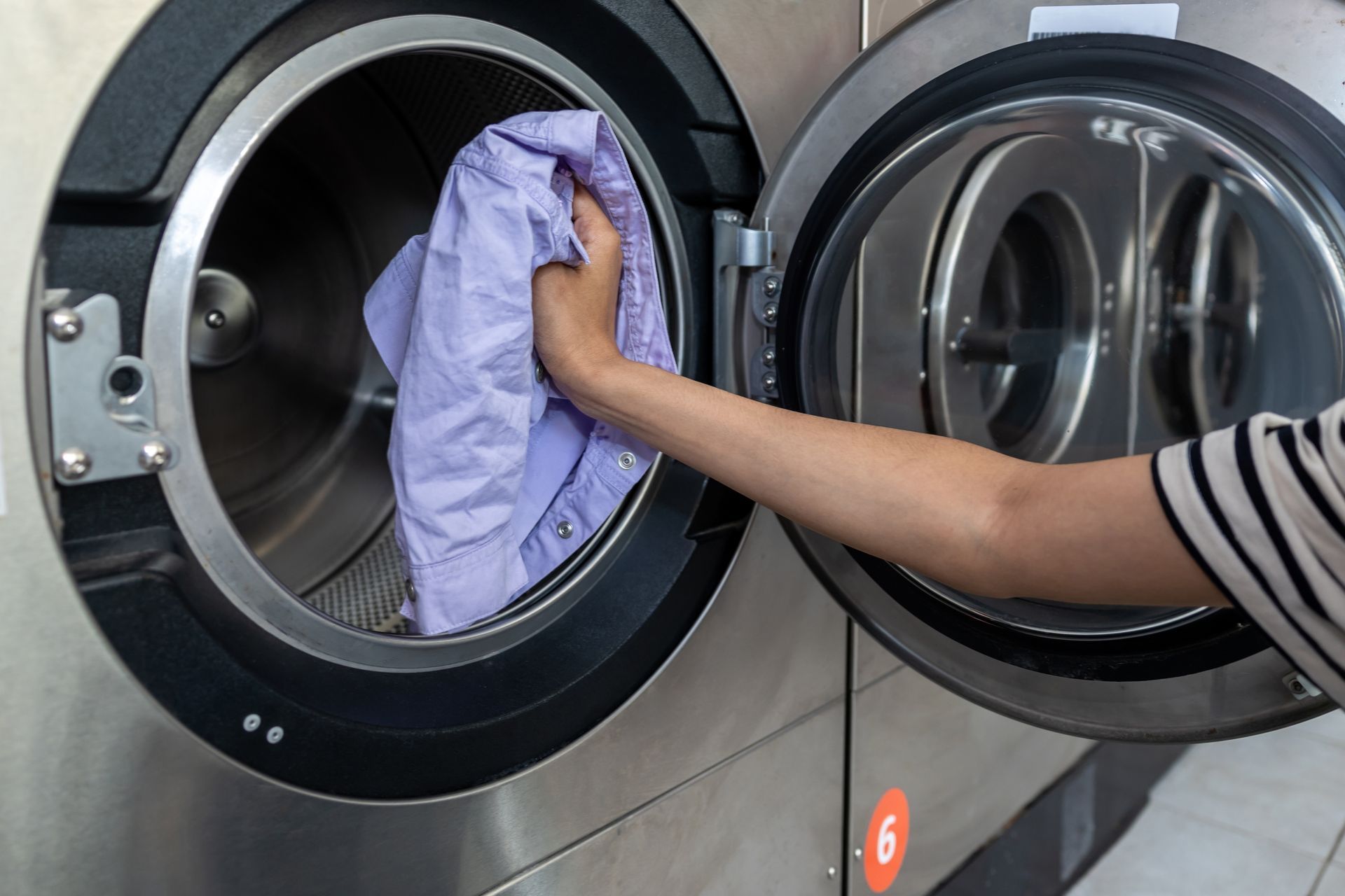 Person putting a purple shirt into an open washing machine in a laundry room