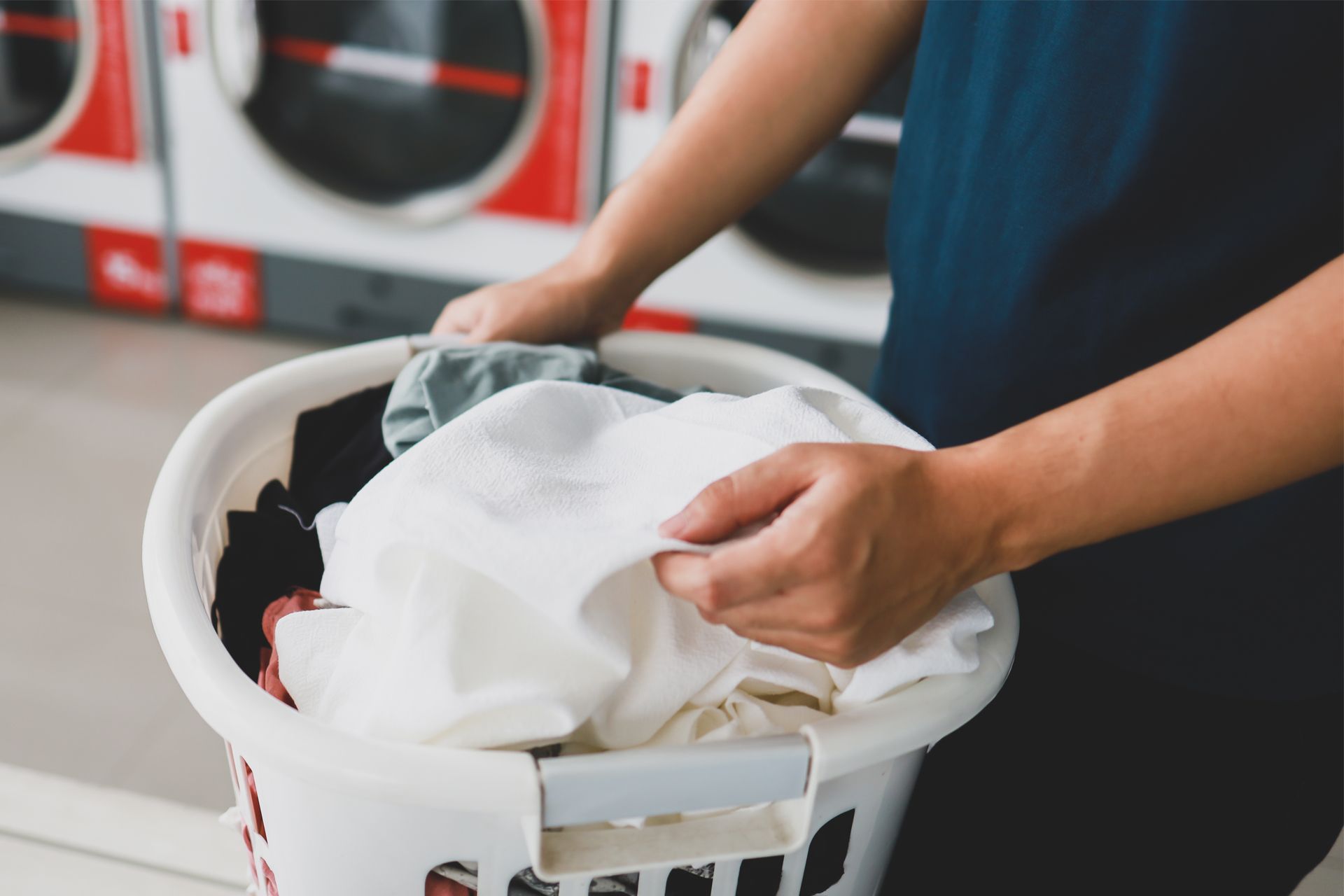 Person holding laundry basket with clothes in laundromat