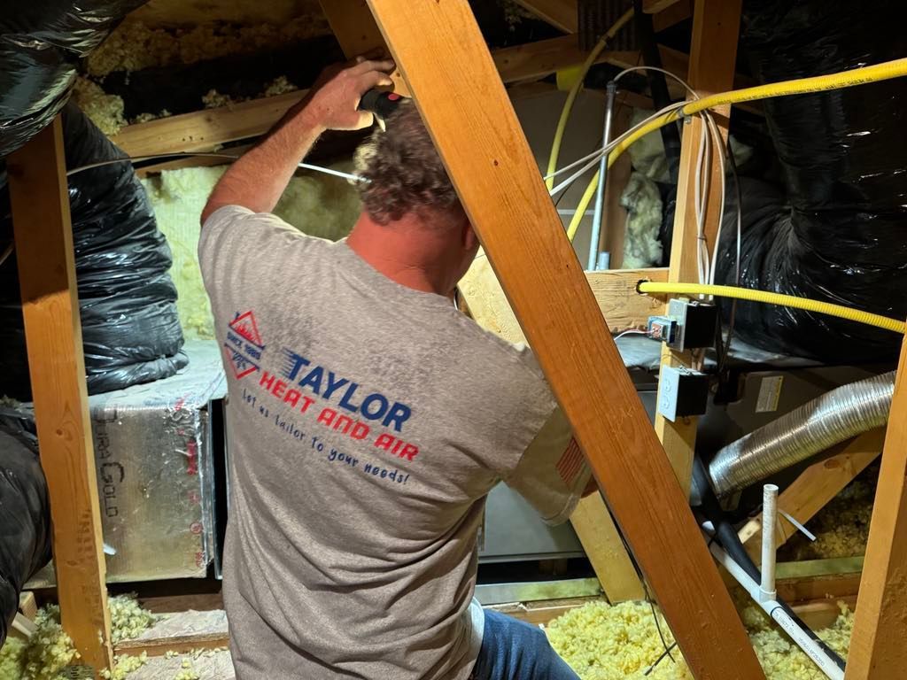 A man is working in an attic with a taylor heat and air shirt on.