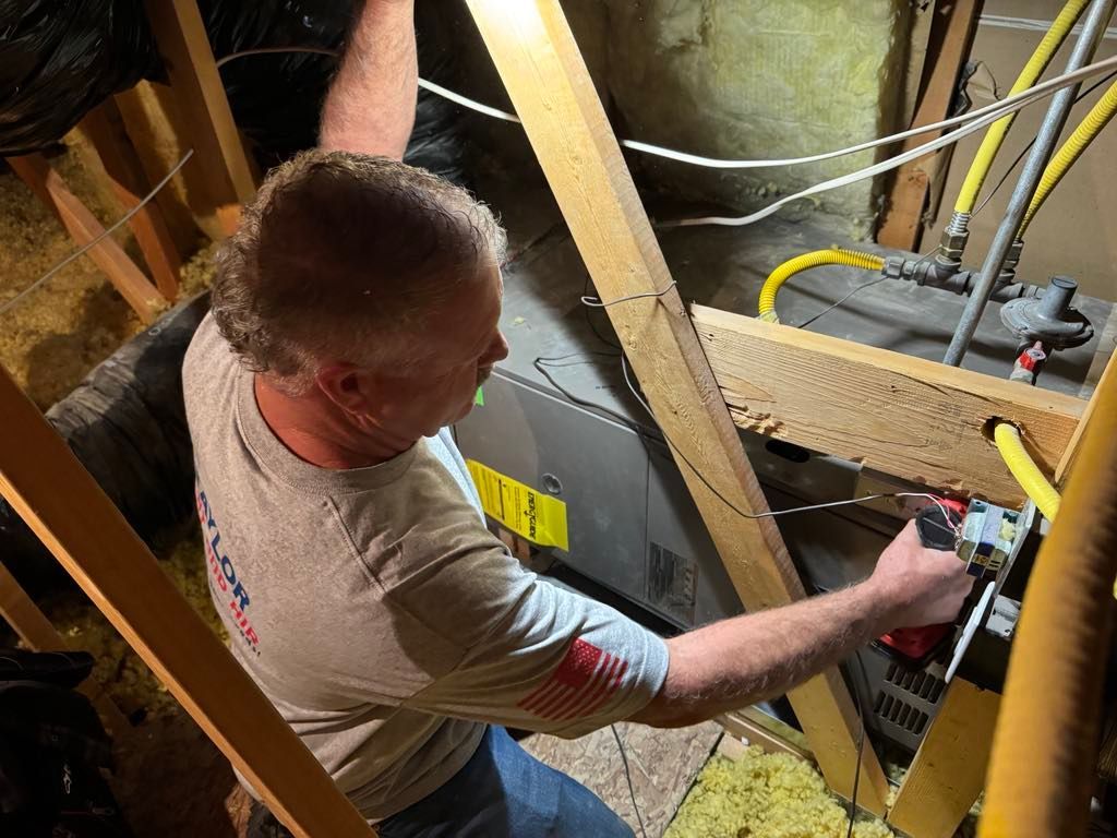 A man is working on an air conditioner in an attic.