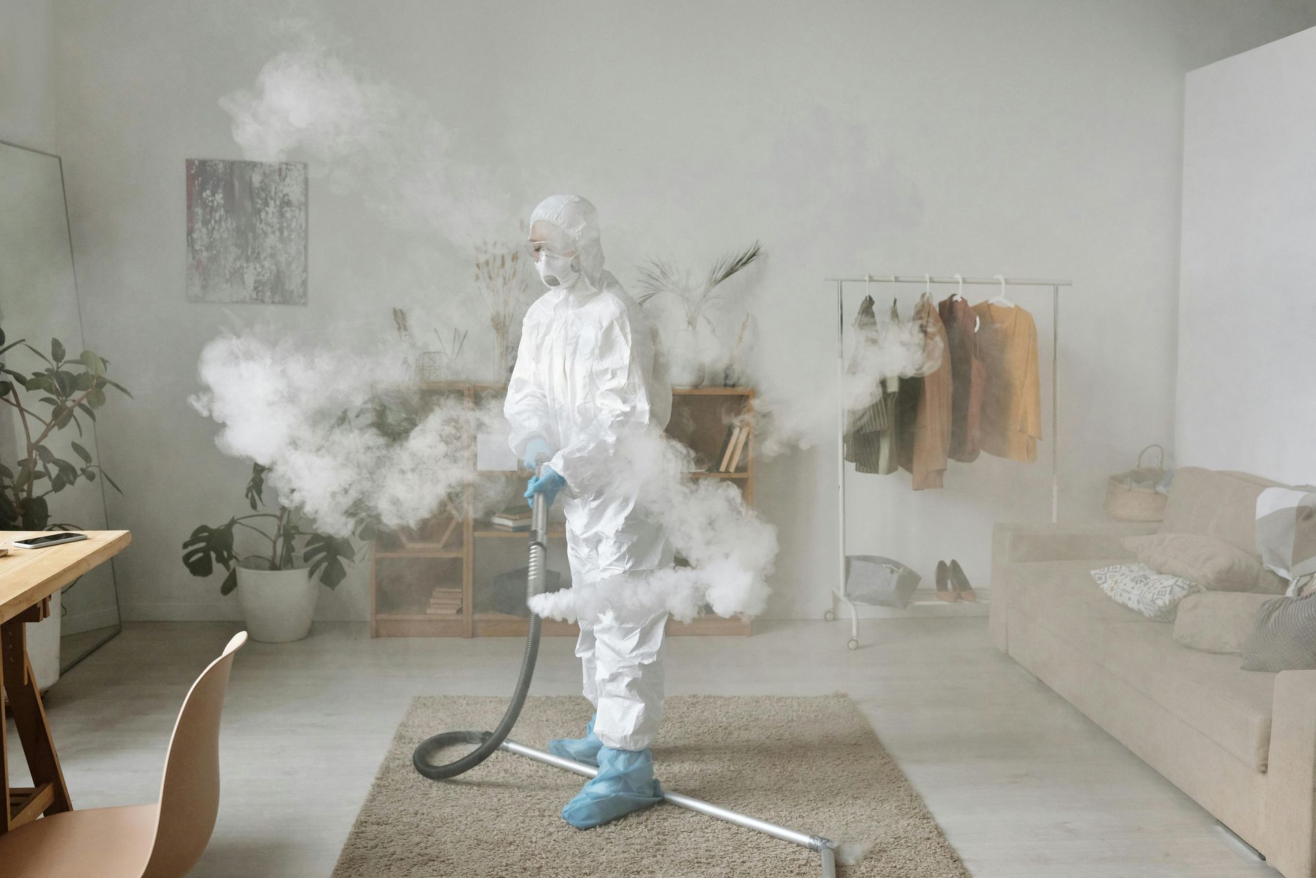 A man in a protective suit is disinfecting a room with a vacuum cleaner.