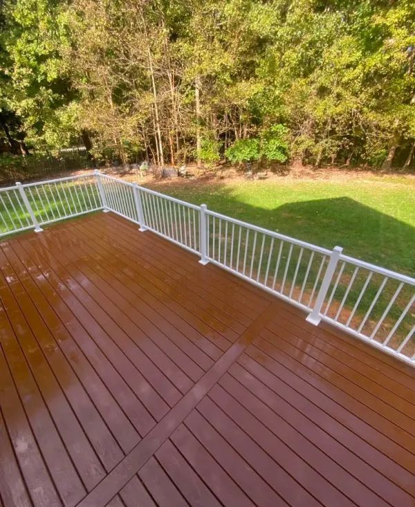 A wooden deck with a white railing and trees in the background