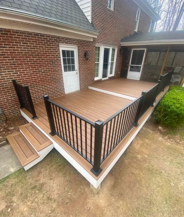 A wooden deck with a black railing is in front of a brick house