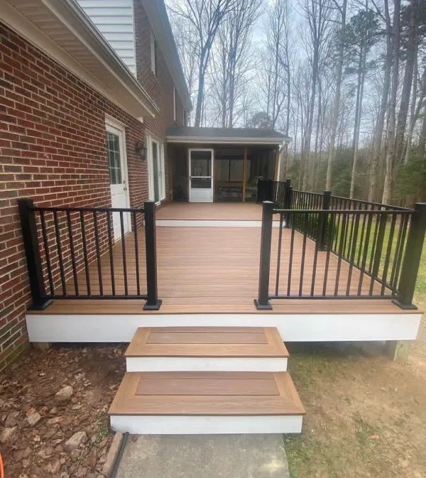 A wooden deck with stairs and a black railing in front of a brick house