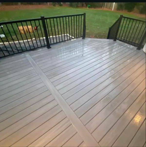 A wooden deck with a black railing and a dog in the background
