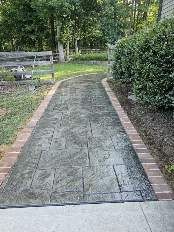 A brick walkway leading to a house with trees in the background