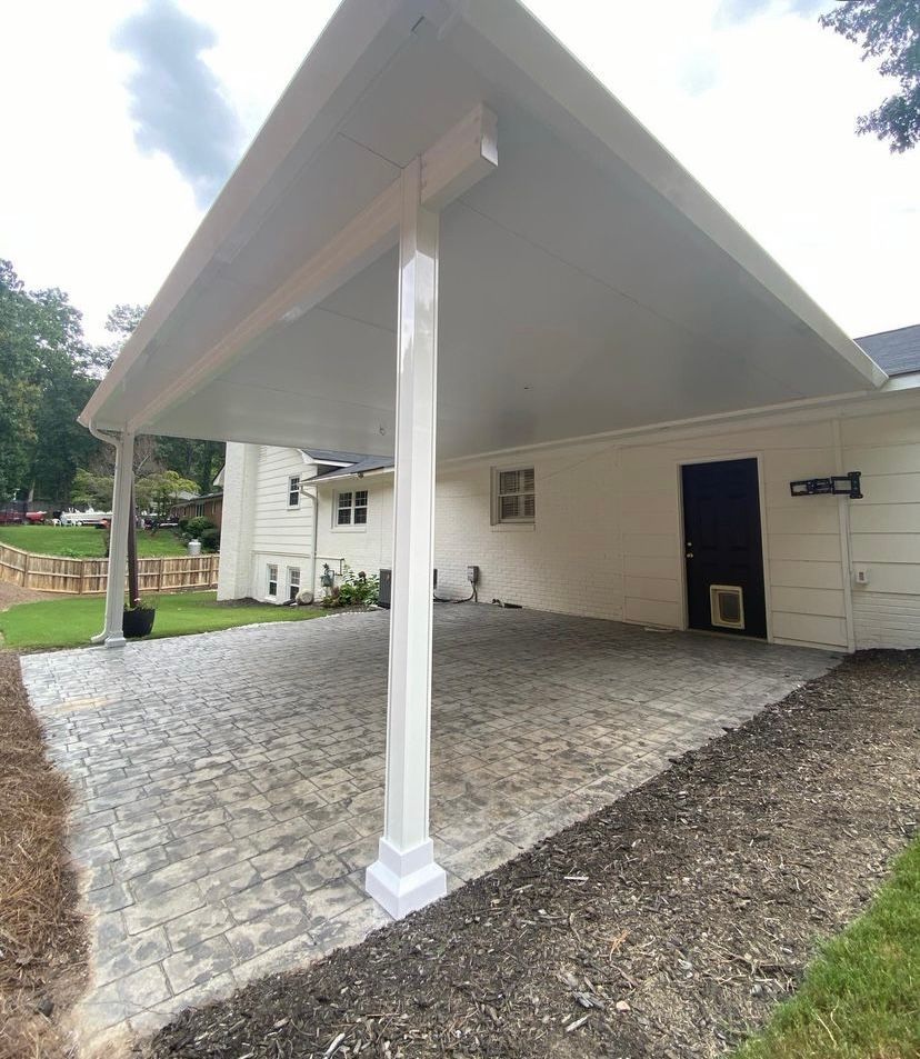A carport with a white roof and a brick driveway in front of a white house