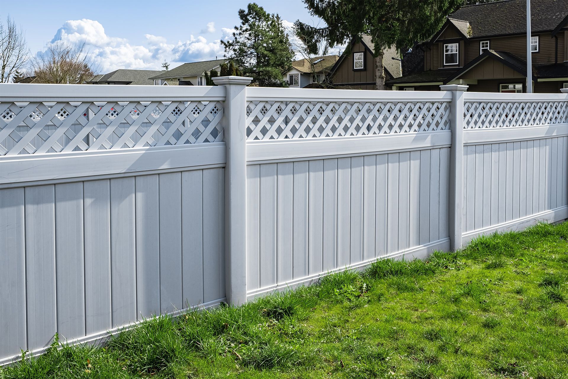 A white privacy vinyl fence surrounds a lush green yard