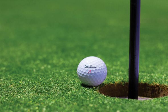 Golf ball near the edge of the hole on a green golf course, with the black flag pole visible.  La Huerta Golf Tournament