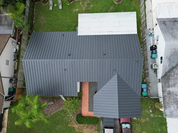 Overhead view of a house with a dark gray metal roof. There is a red brick walkway and a small palm tree.