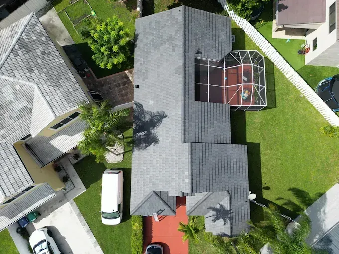 Overhead view of a house with a gray roof and a screened-in pool enclosure, surrounded by green lawns.