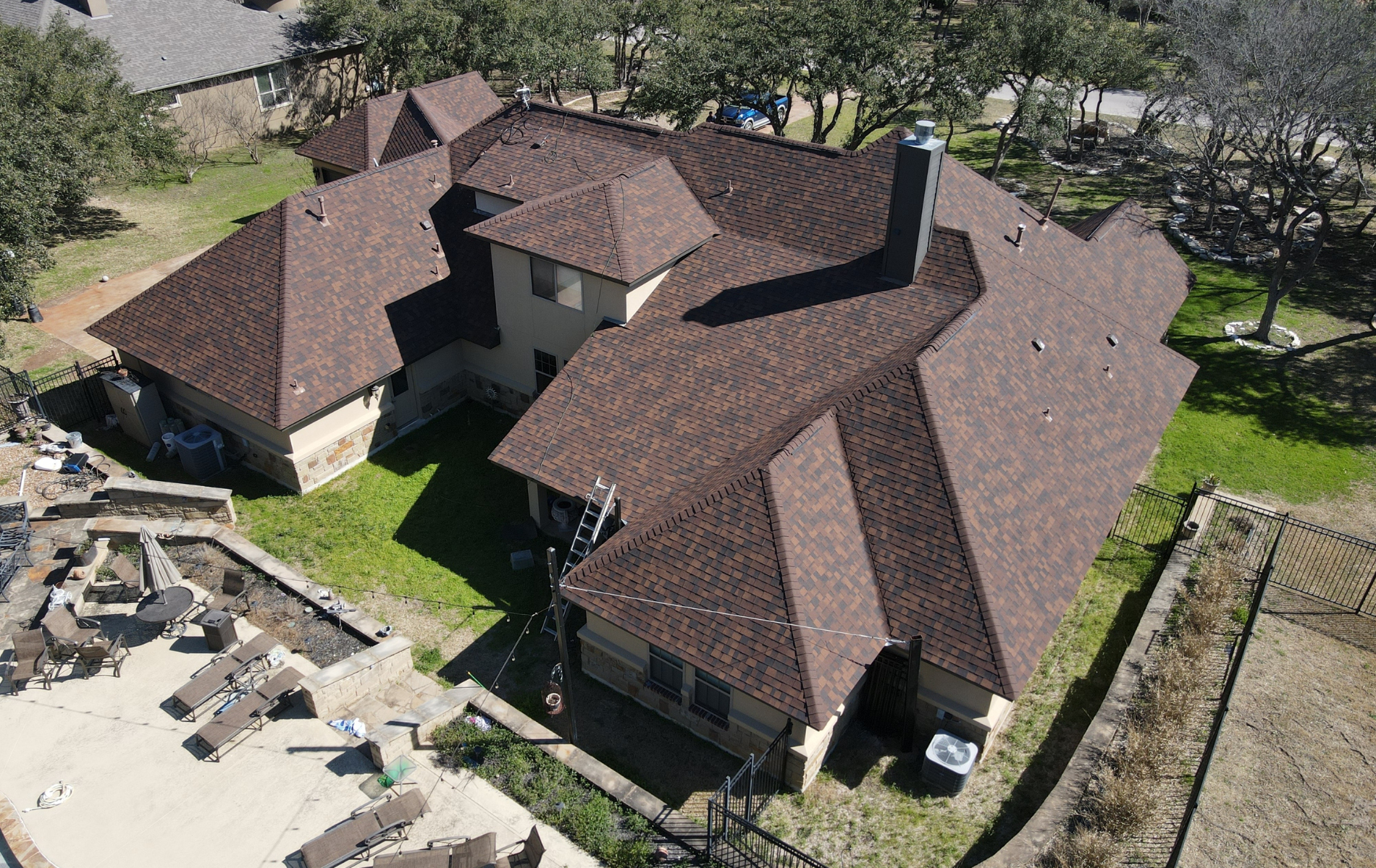 Aerial view of a brown-roofed house with multiple sections and a grassy yard.