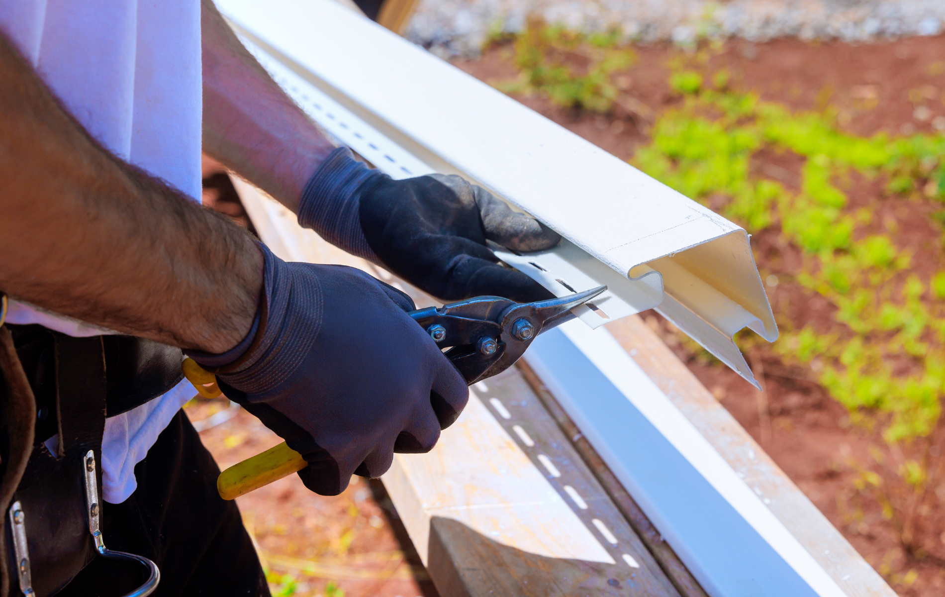 Person in gloves cutting white siding with metal shears outdoors.