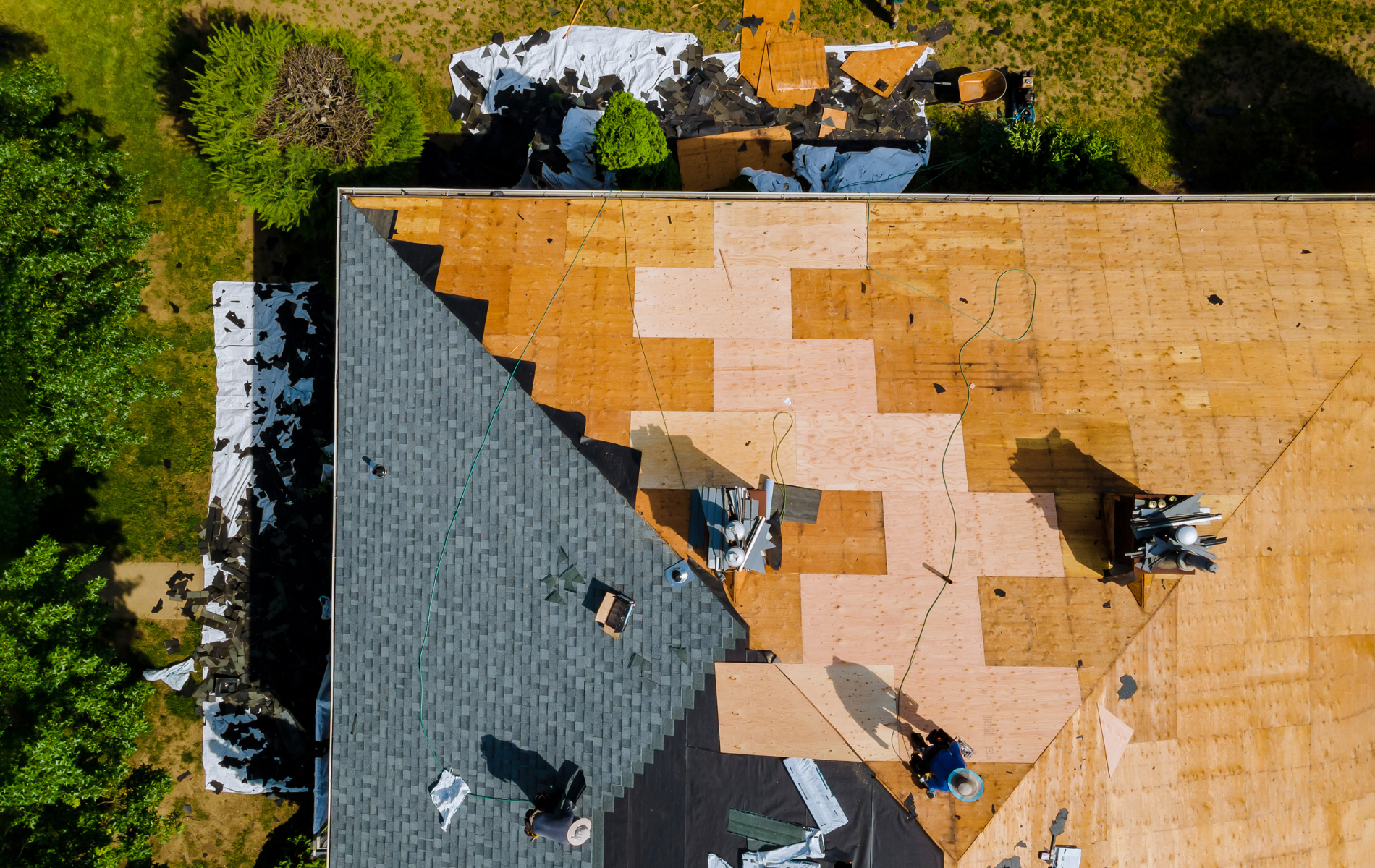 Roof being repaired with workers, asphalt shingles, and exposed wood decking.