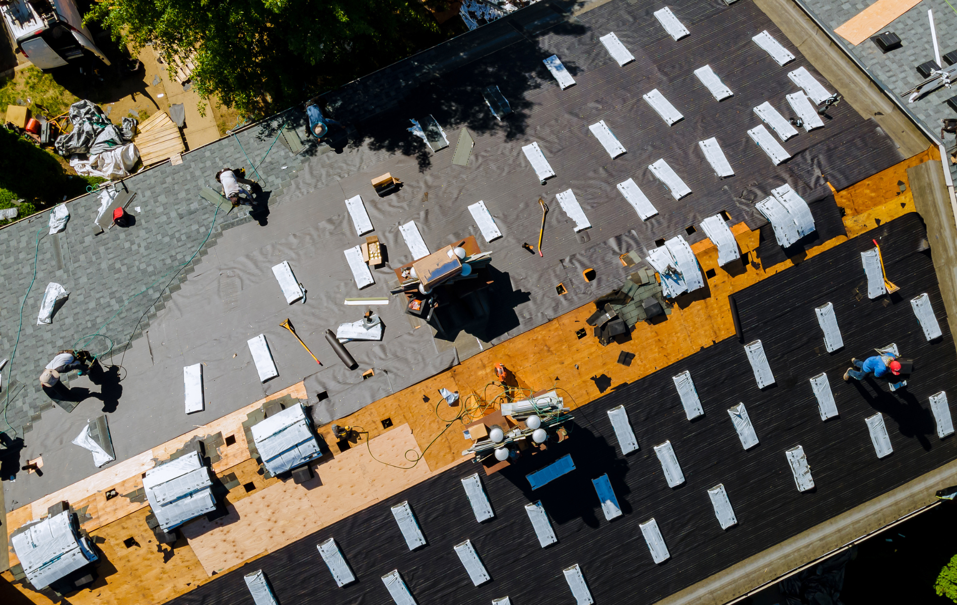 Roofers working on a partially shingled roof, some removing old shingles, some installing new ones; aerial view.