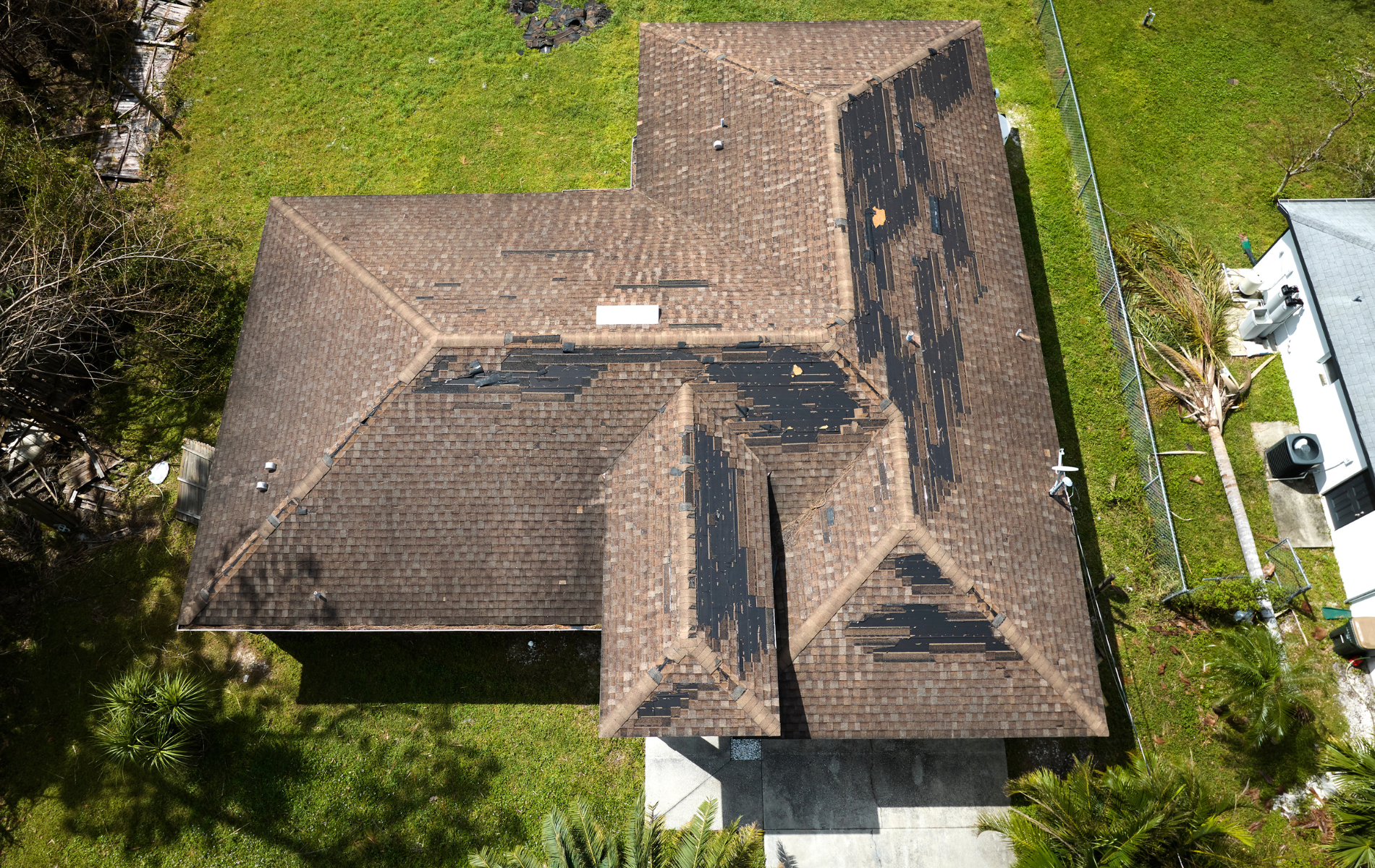 Overhead view of a house with a damaged brown tile roof, surrounded by green grass.