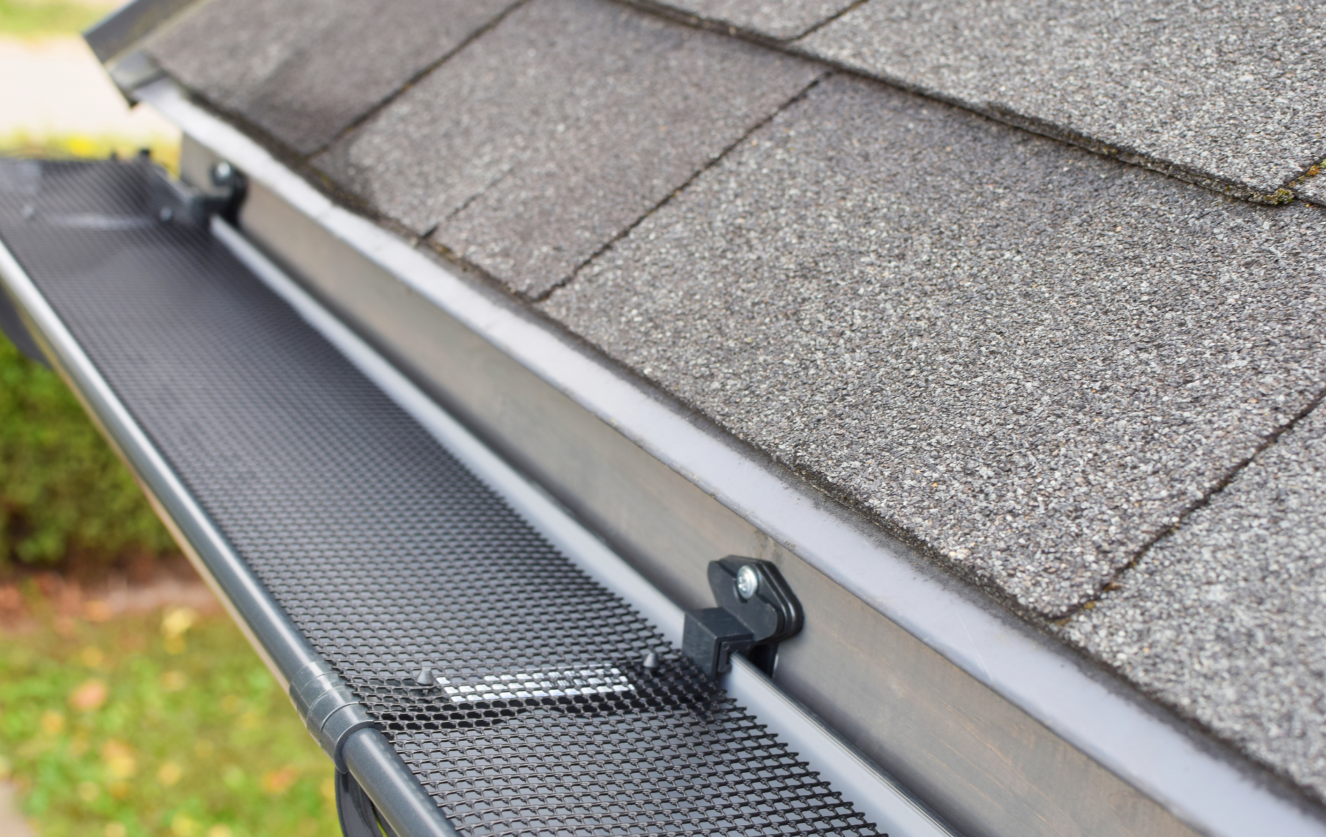Close-up of a gutter with a mesh guard installed on a gray shingled roof.