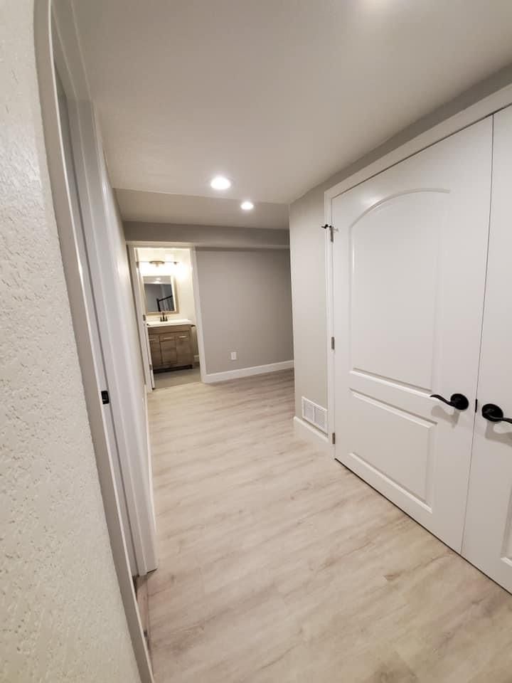 A hallway with hardwood floors and white doors leading to a bathroom.