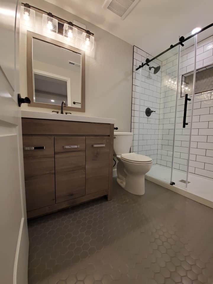 A bathroom with a toilet , sink , mirror and shower.