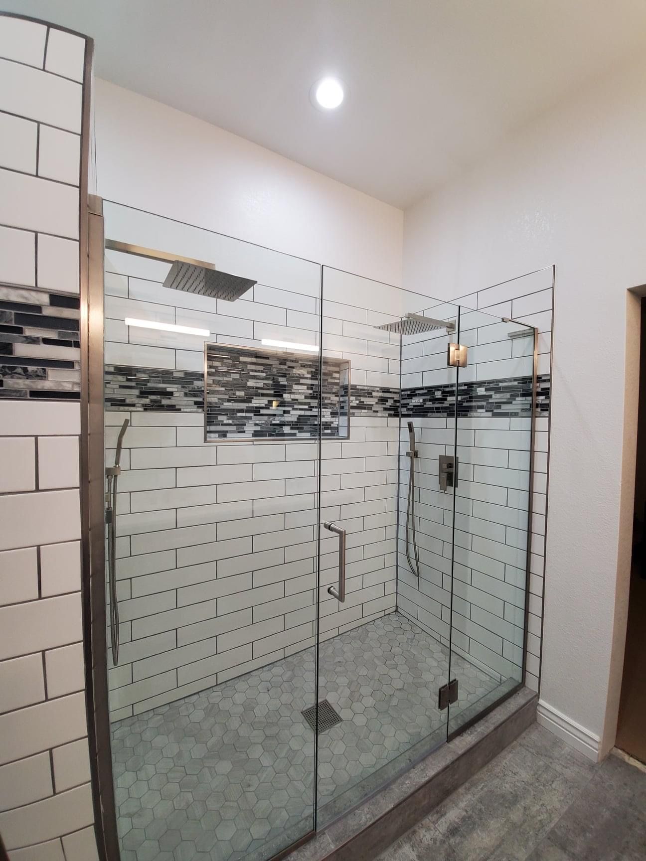 A bathroom with white tiles and a walk in shower with a glass door.