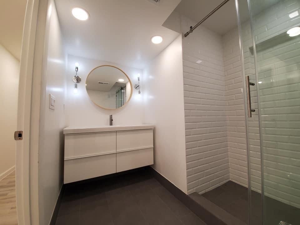 A bathroom with a sink , mirror and walk in shower.