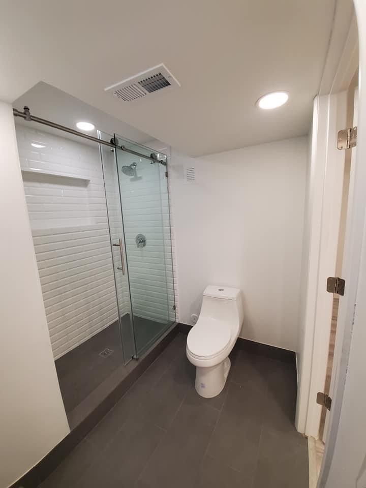 A bathroom with a toilet , shower and sliding glass doors.