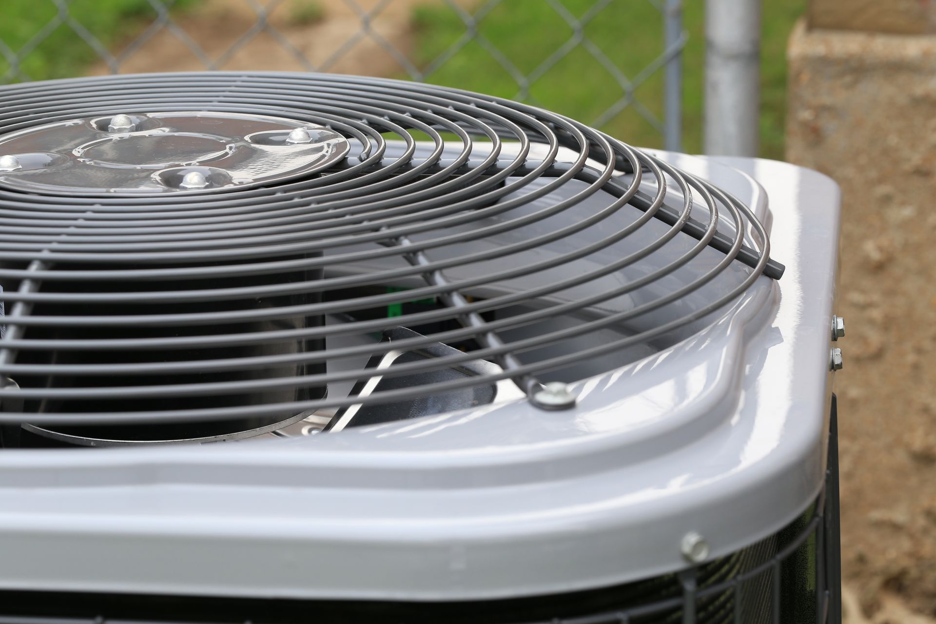 A close up of an air conditioner sitting next to a chain link fence.