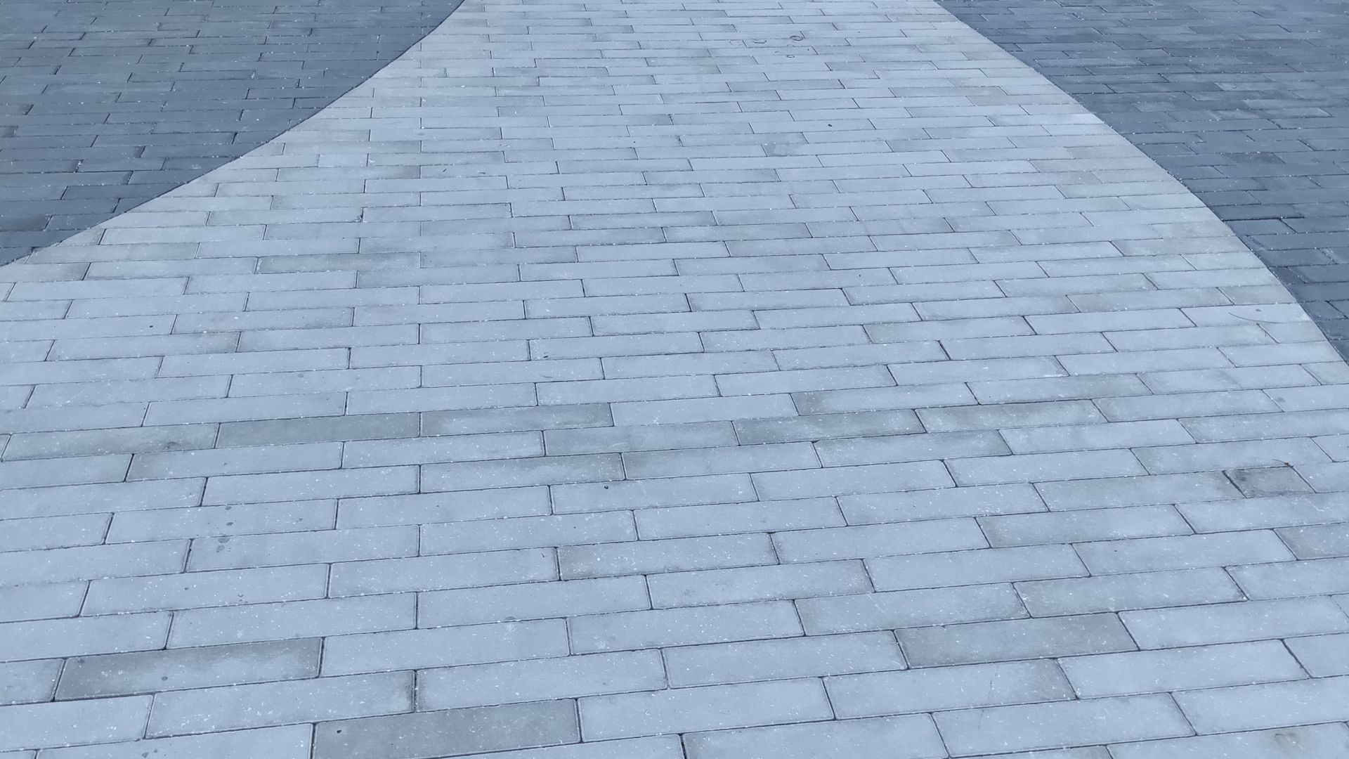 Gray brick pathway curves through gray paved area.