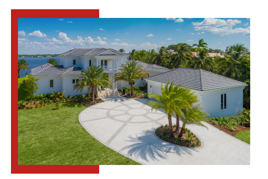 Luxurious white home with a circular driveway, palm trees, and water views.