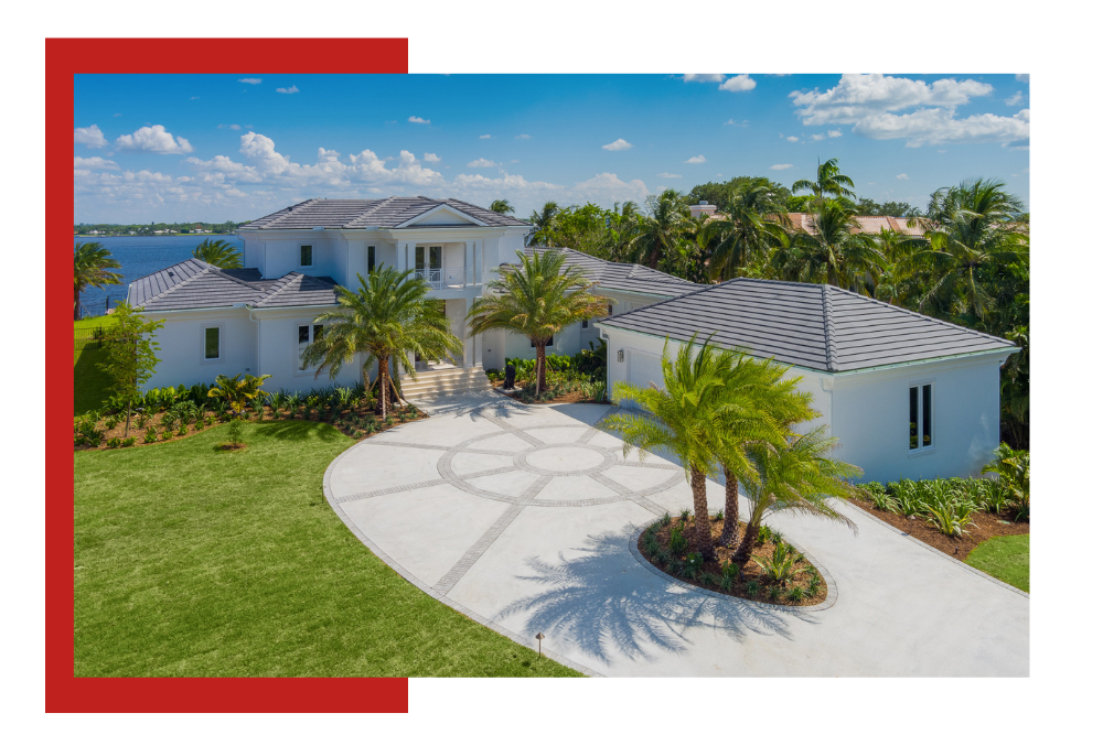 Luxurious white home with a circular driveway, palm trees, and water views.