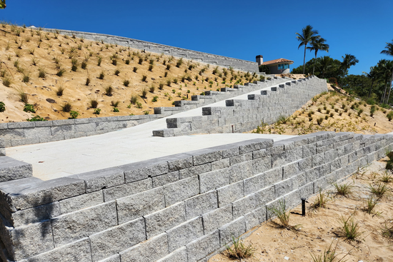 Stone retaining walls and path ascending a hillside with sparse vegetation.