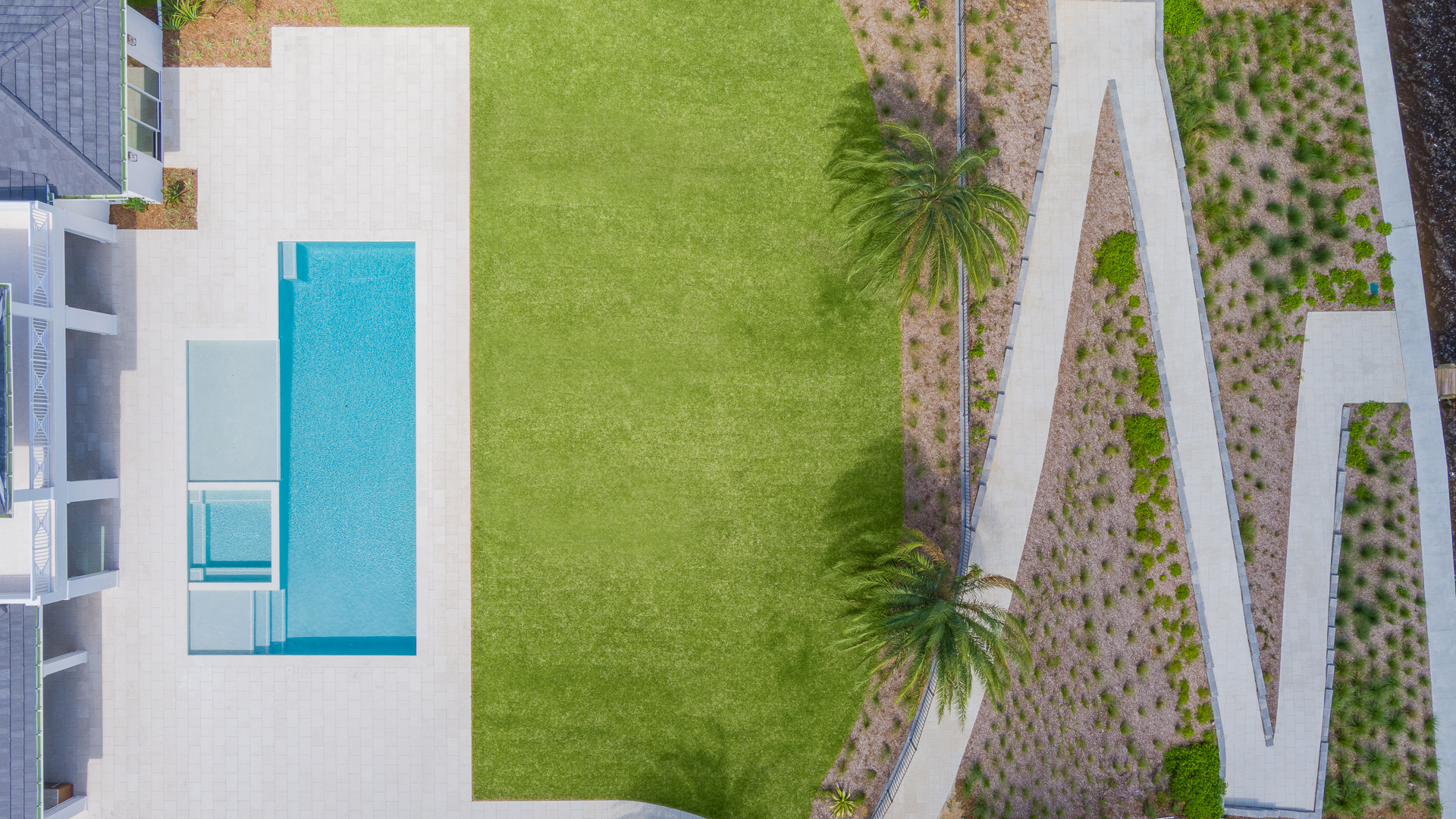 Overhead view of a rectangular pool, green lawn, and white pathway leading to a building.