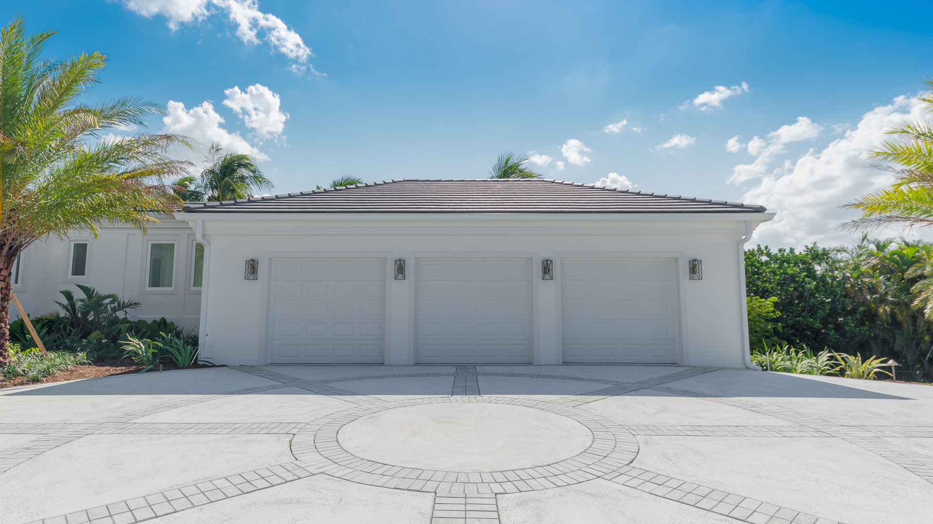 Three-car white garage with gray driveway, palm trees, and blue sky.