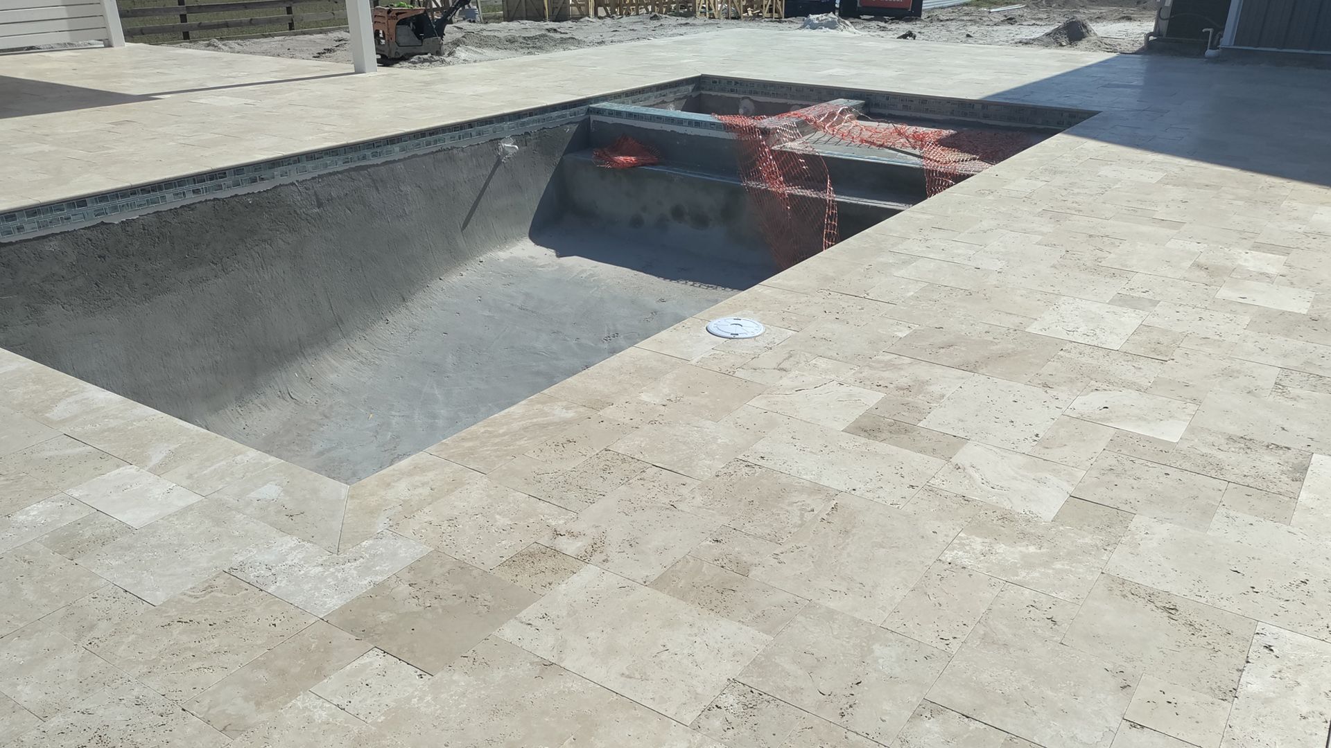 Empty swimming pool under construction, beige tile surround.