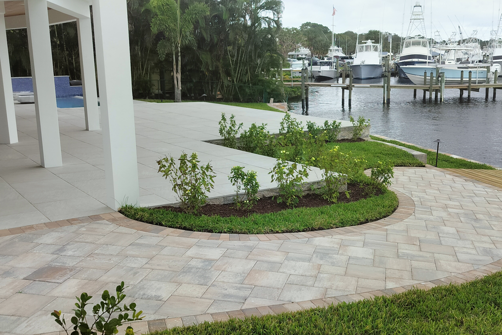 Patio with pavers and green landscaping overlooking a marina with boats.