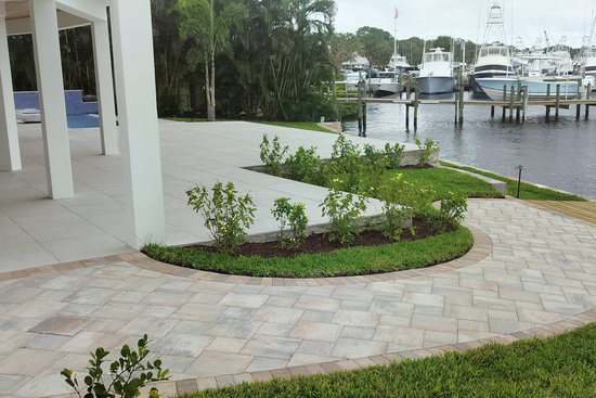 Patio with pavers and green landscaping overlooking a marina with boats.