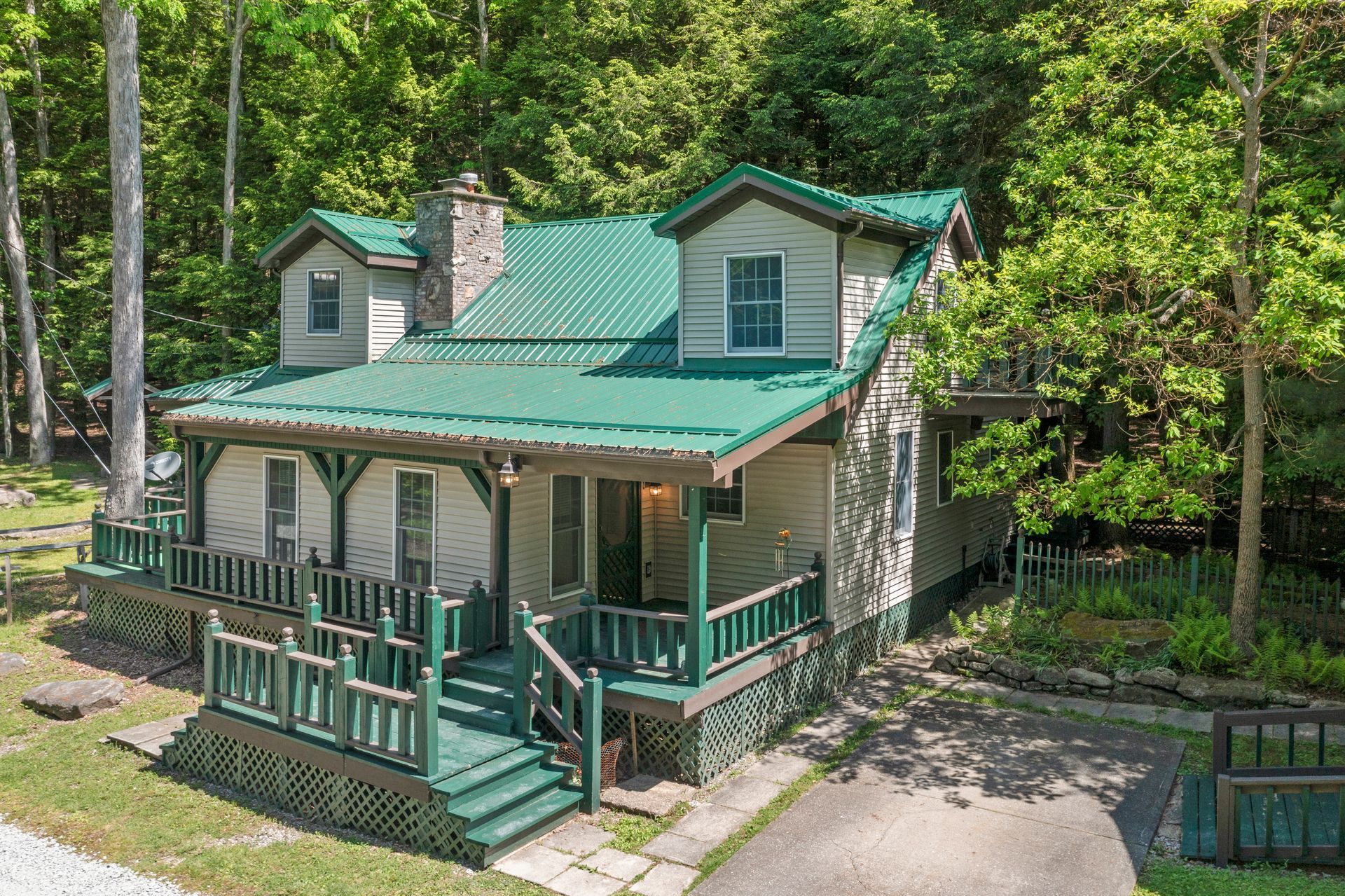 A white house with a green roof and a porch in the middle of a forest.