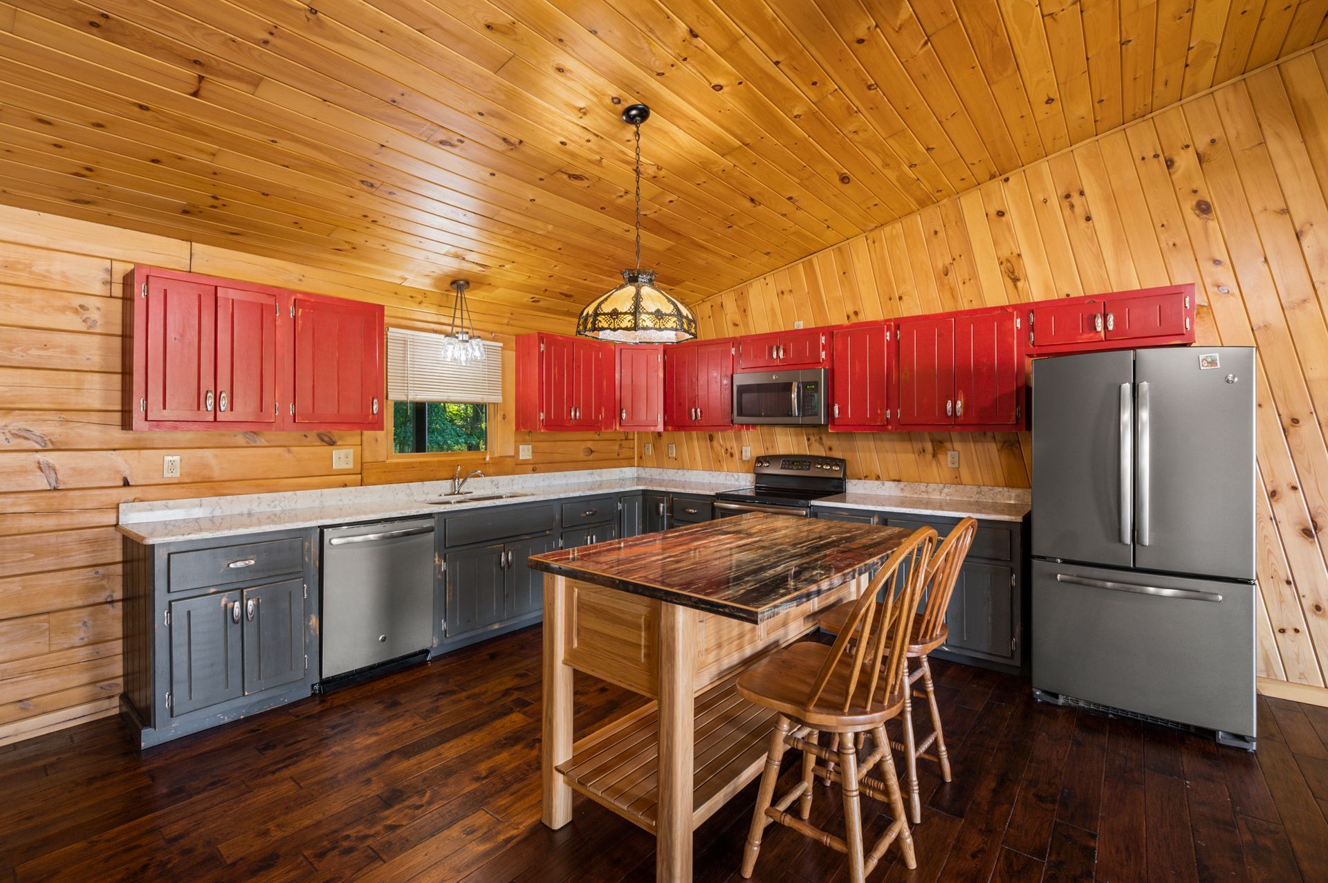 A kitchen in a log cabin with red cabinets and stainless steel appliances.