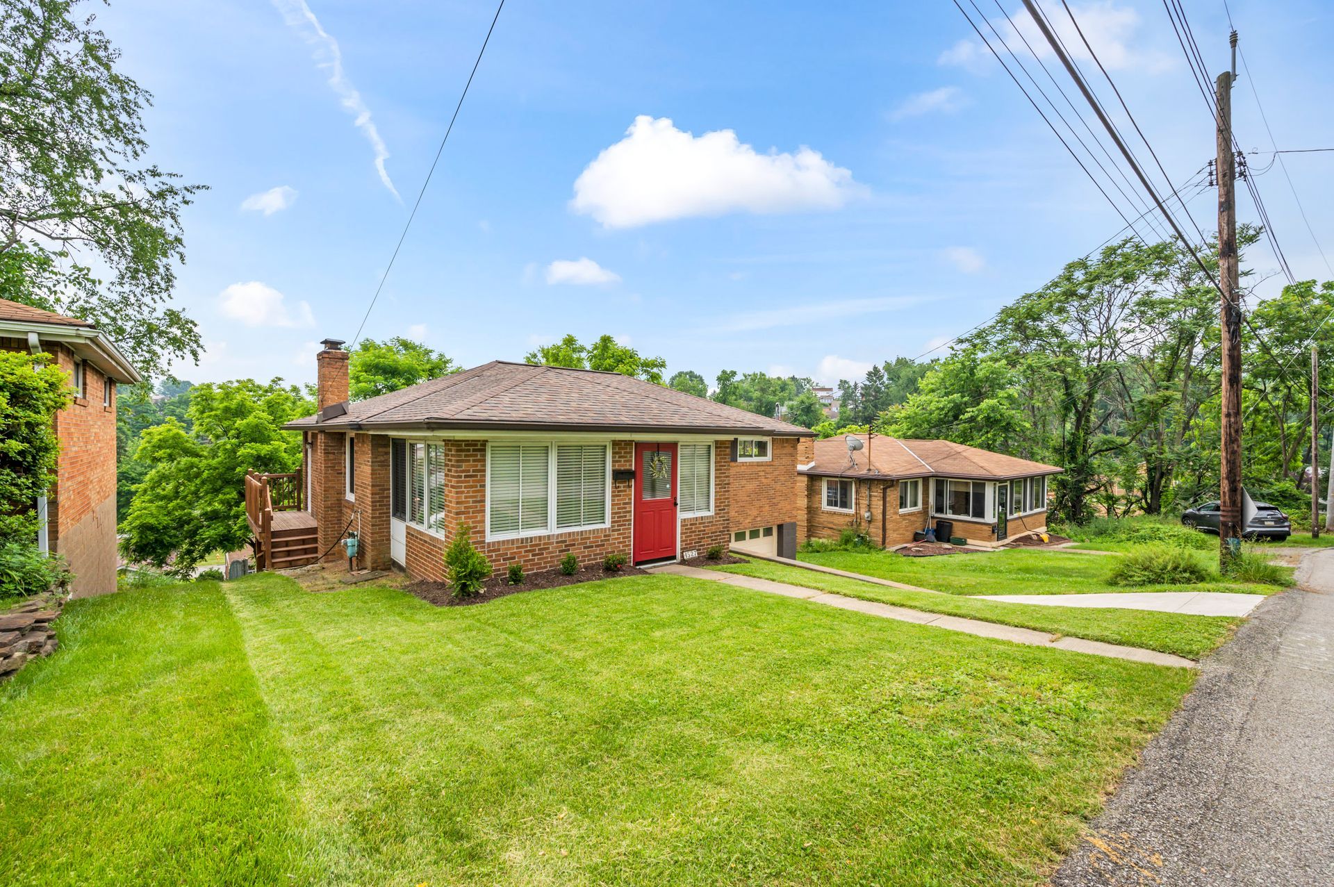 A brick house with a red door is sitting on top of a lush green lawn.