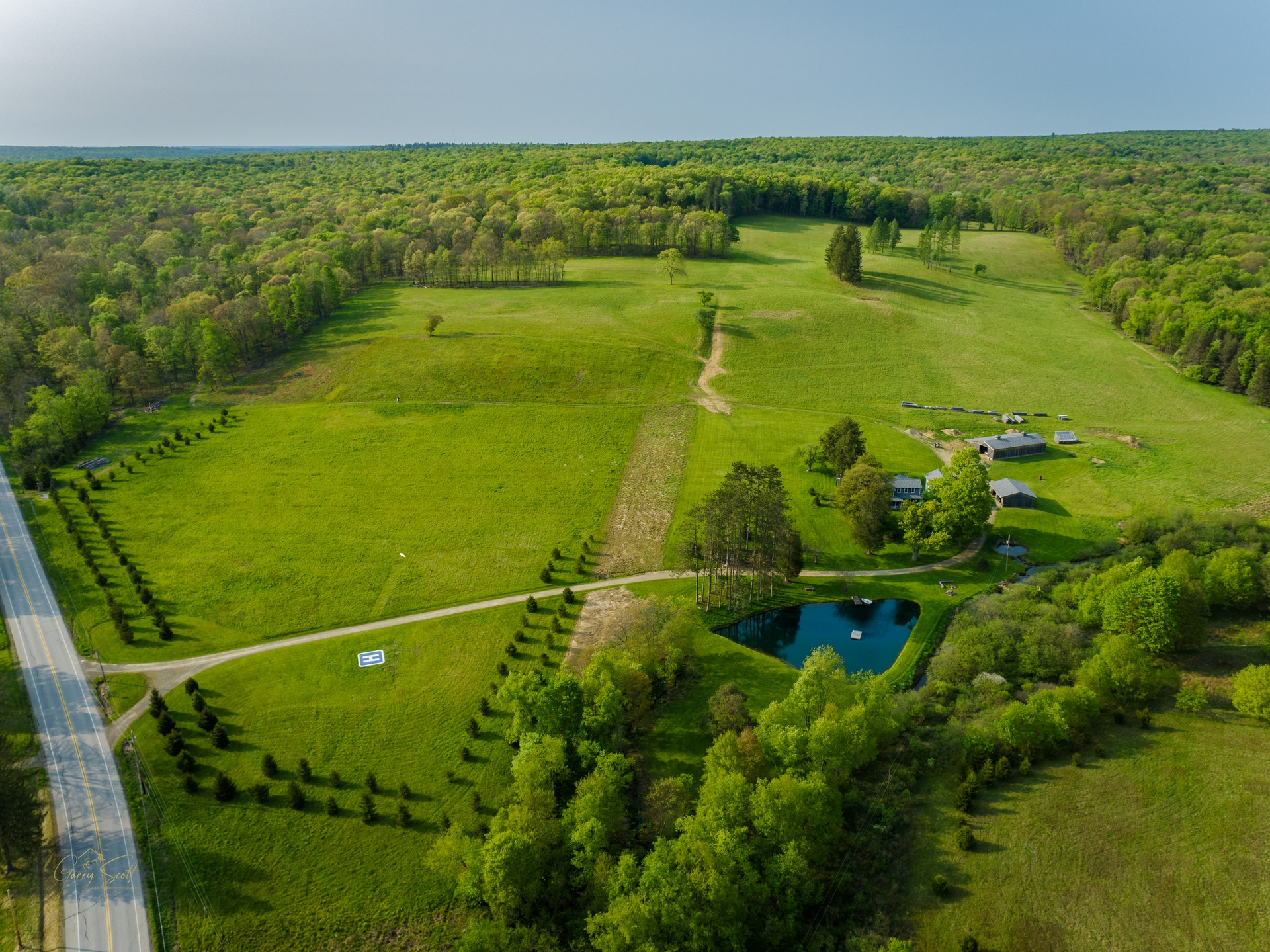 An aerial view of a large green field surrounded by trees and a road.