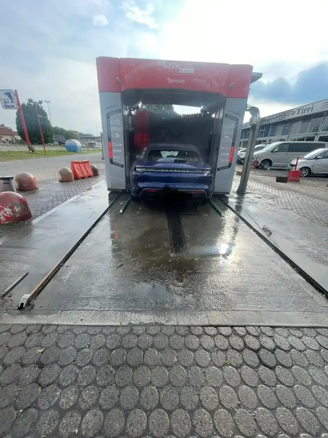 Un'auto blu all'interno di un autolavaggio, mentre viene pulita con getti d'acqua.